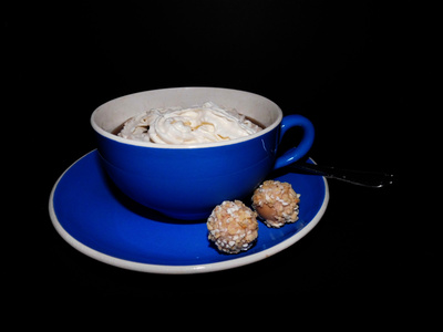 Kaffee in blauer Tasse mit Sahne und Süßigkeit