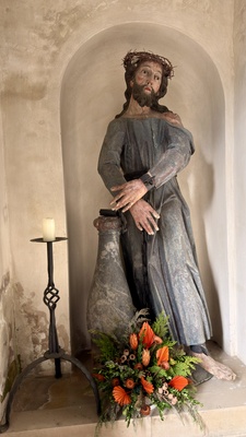 Sp&auml;tgotische Christusfigur mit Dornenkrone in Kirchennische mit Kerze und Blumenschmuck